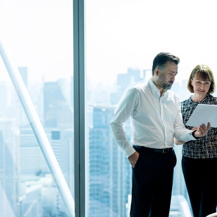 larger image of a man and woman in a high rise office, standing & looking at paperwork